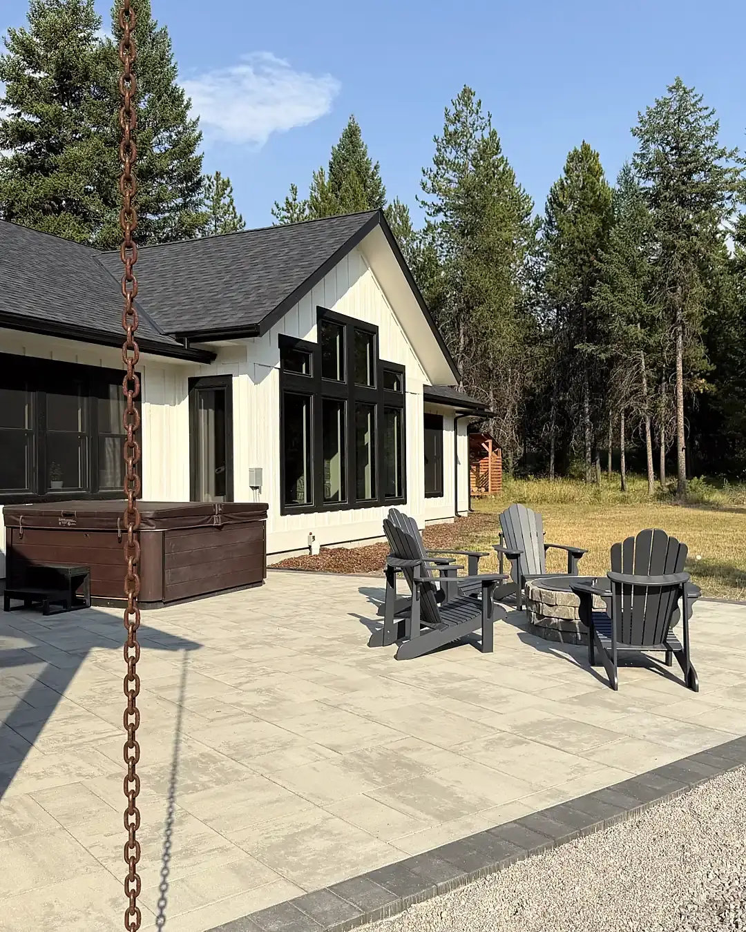 Paver patio with stone fire pit and Adirondack chairs beside a farmhouse